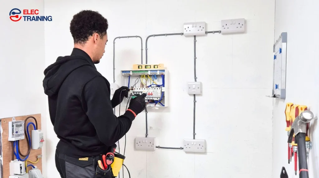 Electrical trainee testing and wiring a consumer unit on a training wall setup during hands-on electrician training.